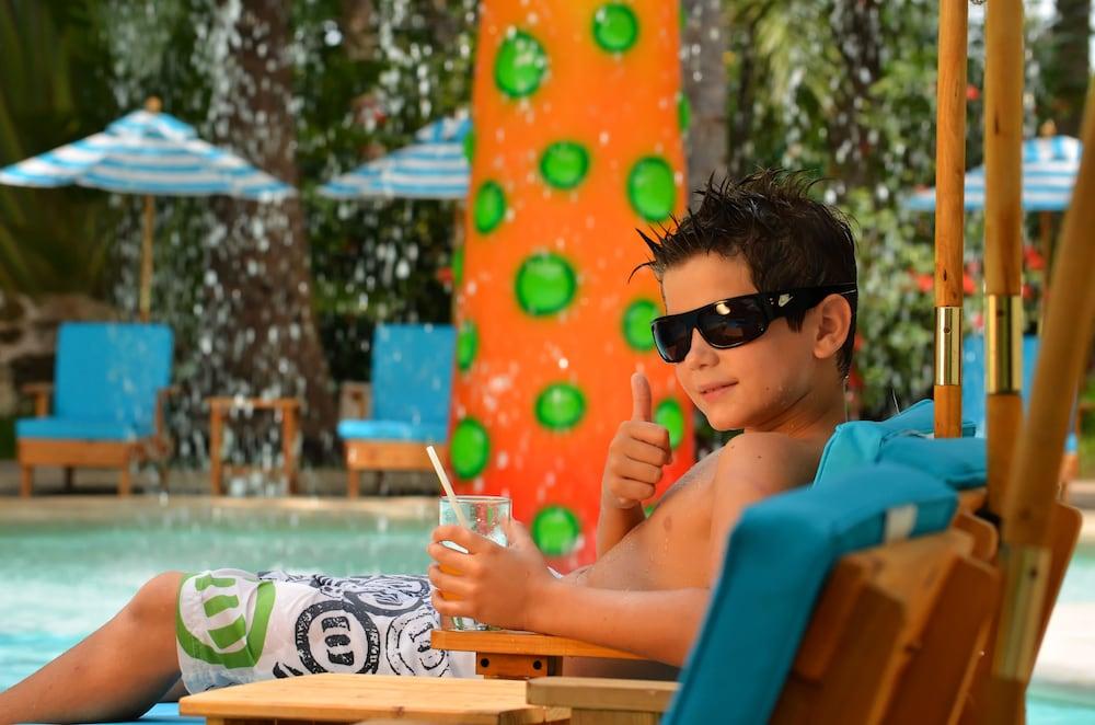 Grand Oasis Palm Ξενοδοχείο Κανκούν Εξωτερικό φωτογραφία The photo shows a young boy relaxing by a pool. He is wearing sunglasses and has a thumbs-up gesture, signaling enjoyment. He appears to be lounging on a chair, holding a drink in a glass. In the background, there is a bright and colorful structure w