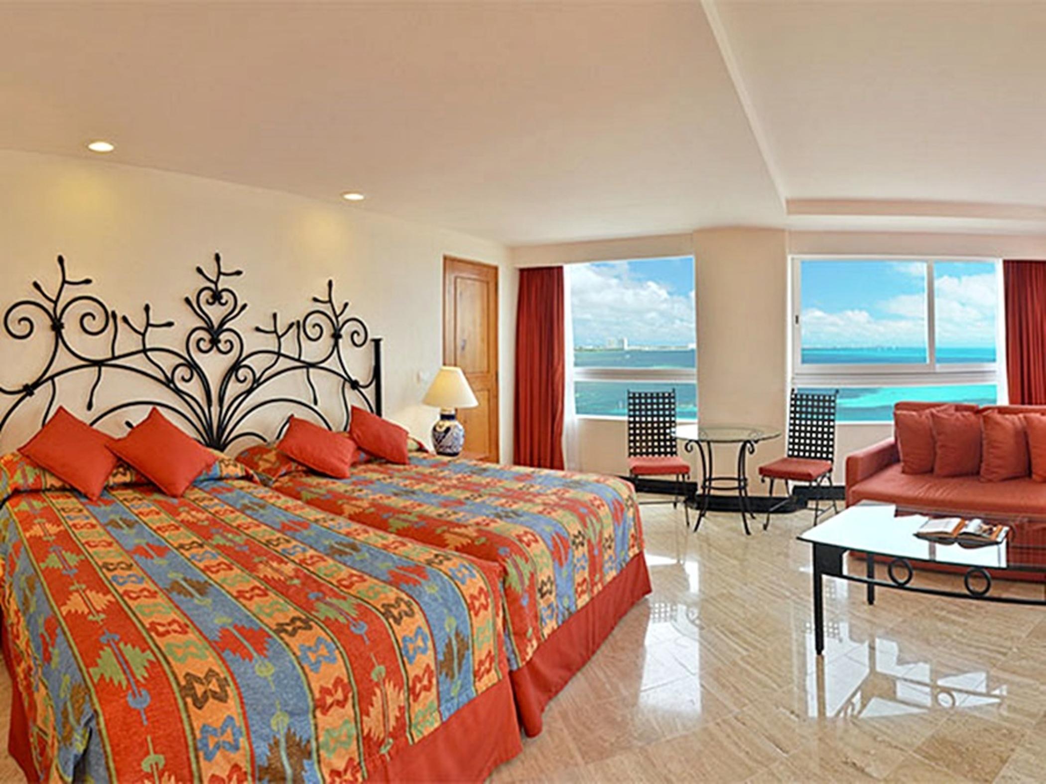 Grand Oasis Palm Ξενοδοχείο Κανκούν Εξωτερικό φωτογραφία The photo shows a spacious hotel room featuring two beds with colorful patterned bedding. The walls are decorated with a decorative iron headboard. There are large windows that provide a view of the ocean and a bright, sunny sky. The room is warmly l
